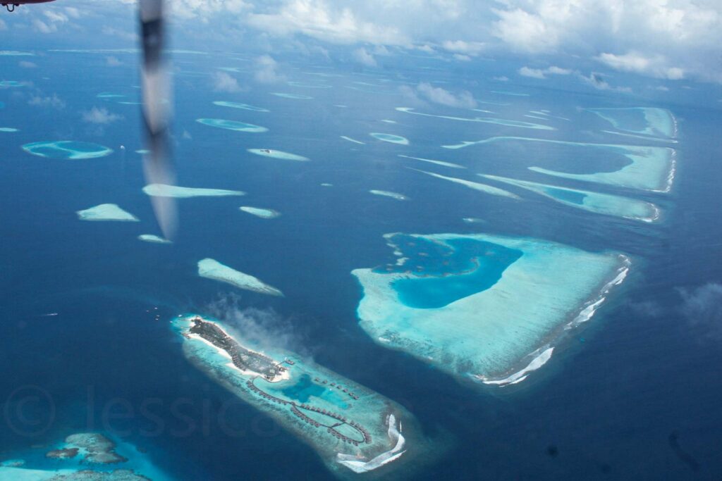 Aerial view from a seaplane of the Maldives atolls, showcasing turquoise and blue waters and luxurious overwater bungalows