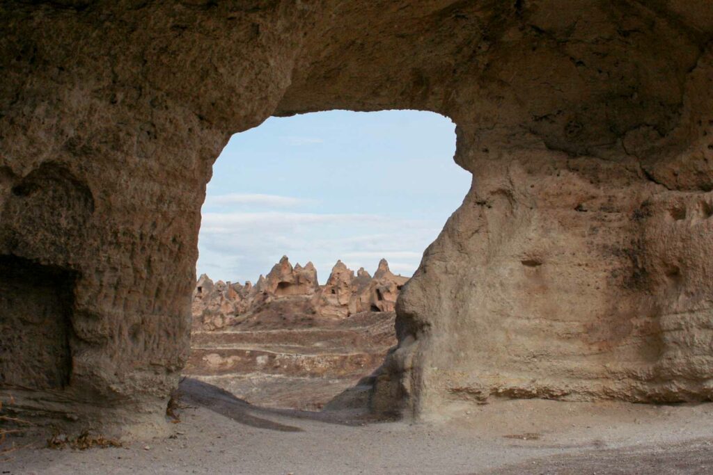 A peek through a cutout in a rock formation looking to the Göreme Open-Air Museum in Cappadocia, Turkey, featuring ancient rock-cut churches and monasteries
