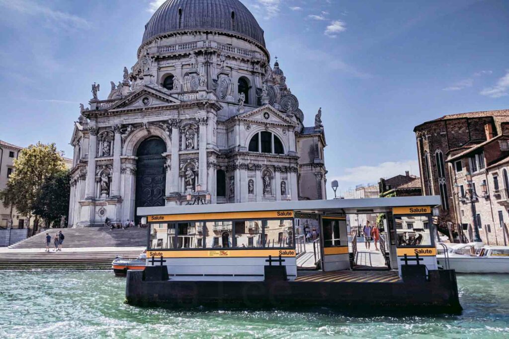 A vaporetto water bus station on the Grand Canal in Venice, Italy, with the majestic Santa Maria della Salute basilica in the background.