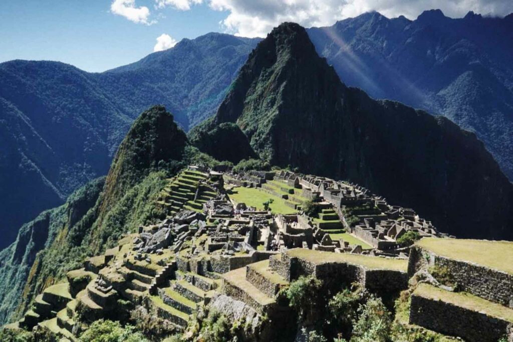 The ancient Incan citadel of Machu Picchu in Peru, nestled among green mountains, under a bright clear summer sky.
