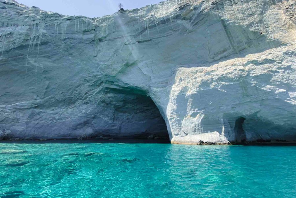 The stunning Kleftiko Caves in Milos, Greece, with crystal-clear aqua teal water and dramatic white cliffs.